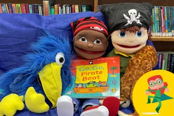 Dolls and puppets are sitting on a chair, holding a children's story book.