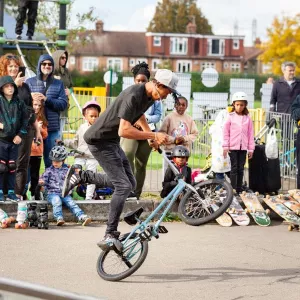 A person performs a BMX move in Chase Lane Skate Park, people around are watching them