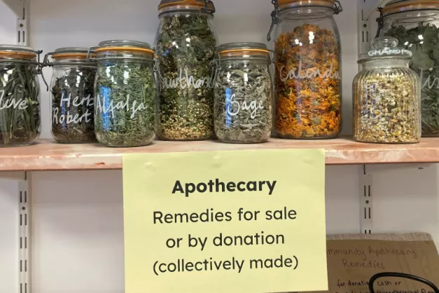Image of various jars of herbs displayed on a shelf, with label that reads 'remedies for sale or by donation'. 