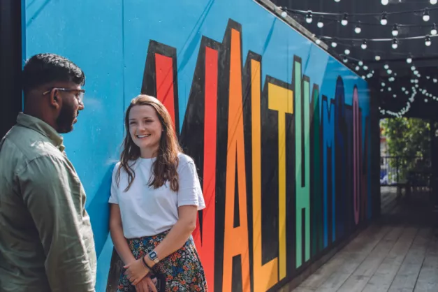 A young man and woman lean against a wall with the word Walthamstow painted on it