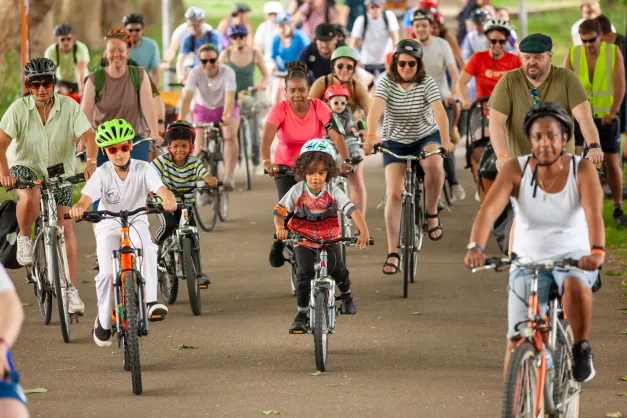 Picture of children and adults on bikes with helmets and hats on riding in one direction on a path