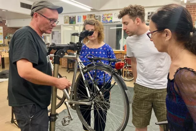 Man fixing a bike with a group of two women and a man observing.