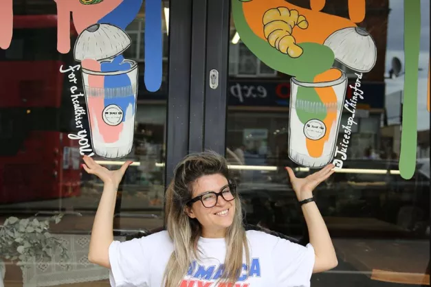 A person smiling with window art holding up two drinks 