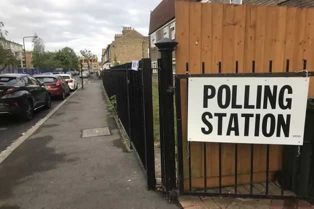 A white sign with text "Polling Station" in black tied to a railing along a foot path