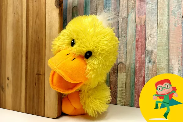 Fluffy hand puppet duck is peeking from behind a wall.