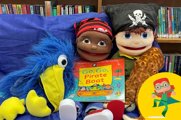 Dolls and puppets are sitting on a chair, holding a children's story book.