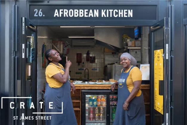Image of two women outside Afrobbean Kitchen, pointing at the sign 