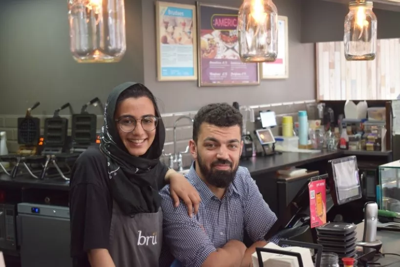 Man with arms crossed with woman in a coffee shop
