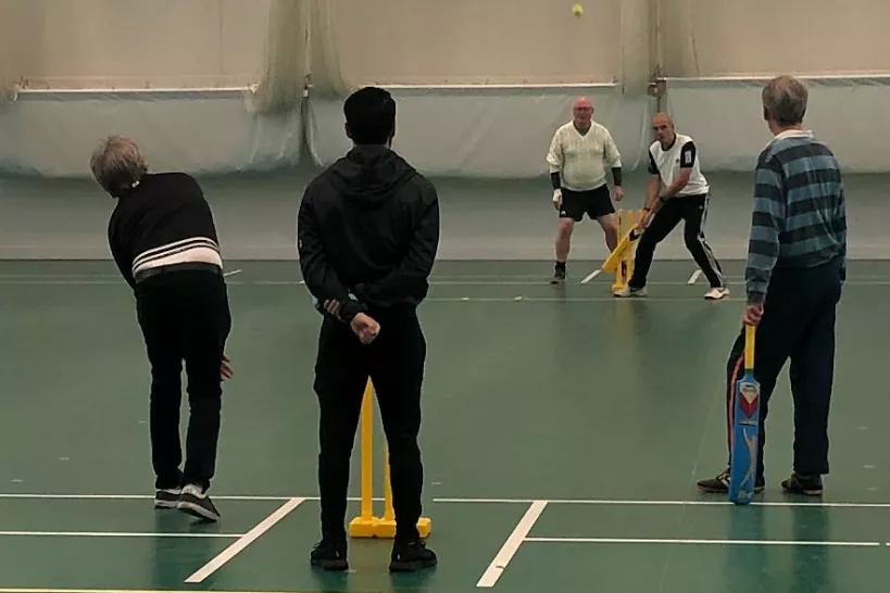 Small group of people playing cricket indoors