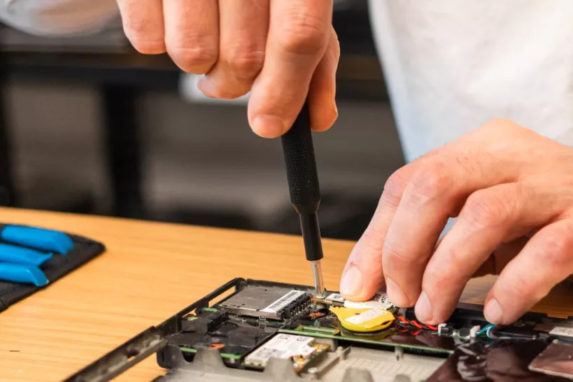 Two hands are shown.  A small tool is being used to fix electronics