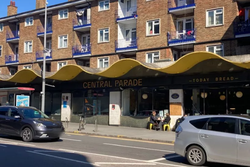 The facade of Central Parade, people are sitting outside a cafe drinking coffee