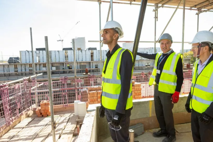 Cllr Khan views the top of the Central Parade building during construction in October 2022. Cllr Khan is standing and looking at the view wearing a hard hat and high vis jacket. Two members of staff wearing PPE are standing next to him. 