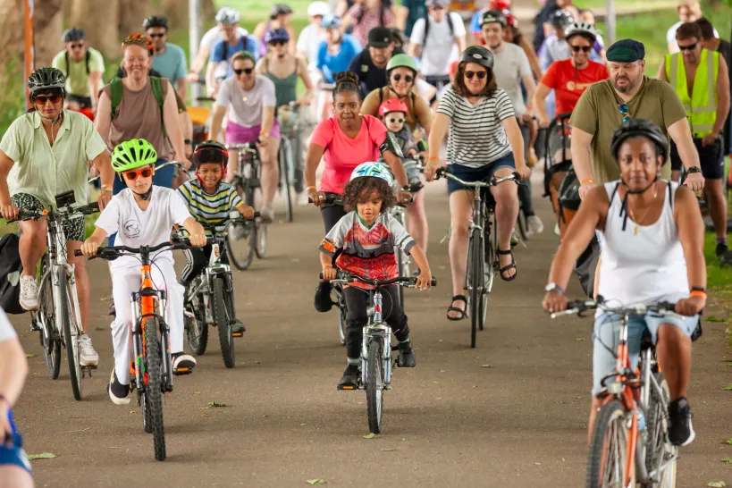 Picture of children and adults on bikes with helmets and hats on riding in one direction on a path