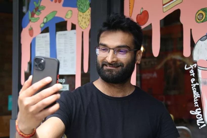 A person smiling taking a selfie in front of a shop window with window art