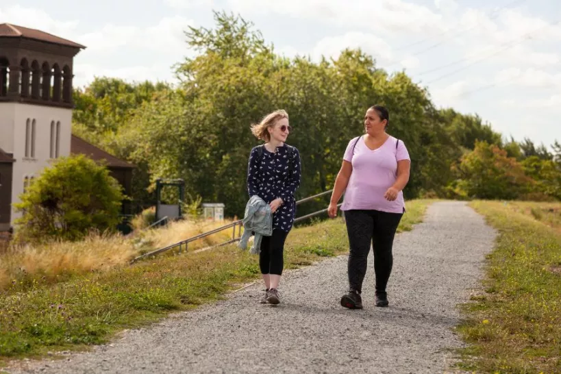 Two women dressed in comfortable clothes walking along one of the paths at Walthamstow Wetlands as they chat