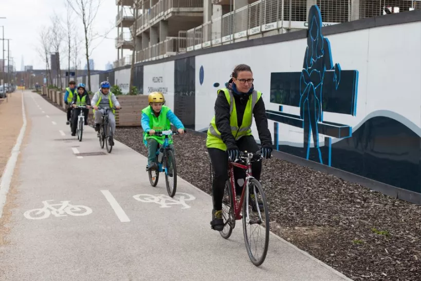 a group of adults and children wearing hi-vis vests cycling on a cycle path in a single file