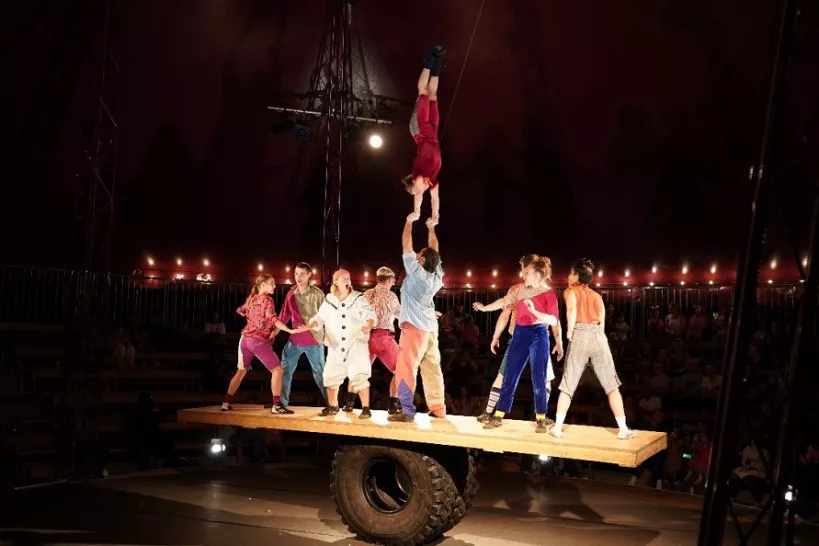Group of children doing acrobats on a plank of wood balanced on a wheel